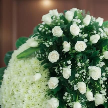 Fotografía macro premium de la Corona Fúnebre Descansa en Paz, mostrando rosas blancas y follaje verde con rocío sutil, profu