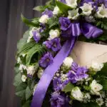 Primer plano de una corona fúnebre 'Homenaje a Daniel' con flores blancas y moradas, follaje verde, cinta satinada morada con