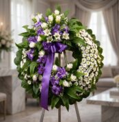 Corona fúnebre 'Homenaje a Daniel' con flores blancas y moradas, cinta de raso morada, sobre un caballete en una sala de vela