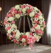 Corona fúnebre Homenaje a Jesús con rosas rosadas, claveles y crisantemos blancos, sobre un caballete en una sala de velación