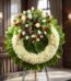 Corona fúnebre "Legado de Hildegarda" con rosas blancas y rojas, crisantemos blancos y follaje verde, en sala de velación pre