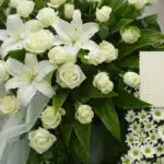 Corona fúnebre Legado Jacob con rosas blancas, lirios y margaritas, rocío sutil, cinta satinada y sobre de condolencias en un