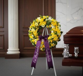 Corona fúnebre de flores amarillas y blancas con cinta morada "En Profunda Simpatía" junto a un ataúd en sala de velación ele