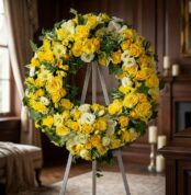 Corona fúnebre Legado de Paz para Benjamin, con rosas amarillas, flores blancas y follaje verde, exhibida en una sala de vela