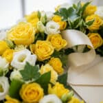 Fotografía macro premium de la Corona Fúnebre Legado de Paz para Benjamin, con rosas amarillas y blancas, follaje verde, rocí