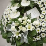 Primer plano de una corona fúnebre "Legado de Paz" con lirios blancos, margaritas y anthuriums, follaje verde oscuro con rocí