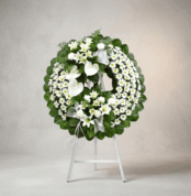 Corona fúnebre Legado de Paz con flores blancas, lirios, margaritas y anturios, sobre un caballete blanco en un fondo elegant