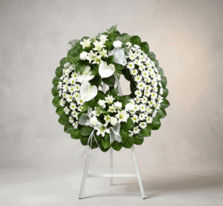 Corona fúnebre Legado de Paz con flores blancas, lirios, margaritas y anturios, sobre un caballete blanco en un fondo elegant