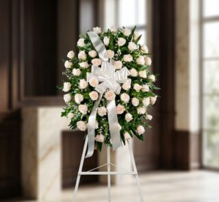 Corona fúnebre Serenidad con rosas blancas y follaje verde, lazo blanco, sobre un trípode en una sala de velación premium con
