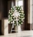 Corona fúnebre Serenidad con rosas blancas y follaje verde, lazo blanco, sobre un trípode en una sala de velación premium con