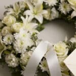 Fotografía macro premium de la Corona Fúnebre Solemne Homenaje Joshua, con texturas hiperrealistas de pétalos blancos y folla