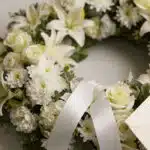 Fotografía macro premium de la Corona Fúnebre Solemne Homenaje Joshua, con texturas hiperrealistas de pétalos blancos y folla