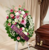 Imponente corona fúnebre "Homenaje a Mathias" con lirios blancos y rosados, gerberas y follaje verde, junto a un ataúd en sal