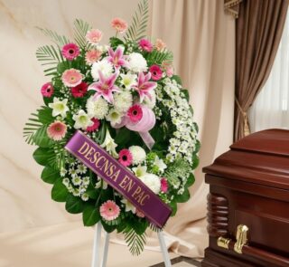 Imponente corona fúnebre "Homenaje a Mathias" con lirios blancos y rosados, gerberas y follaje verde, junto a un ataúd en sal