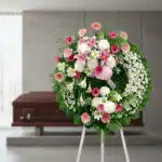 Corona fúnebre solemne 'Homenaje a Mathias' con flores blancas, rosas y follaje verde, en una sala de velación moderna con at