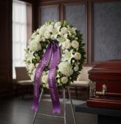 Impresionante corona funeraria de rosas blancas y lirios, con cinta morada de condolencias, en una sala de velación premium j