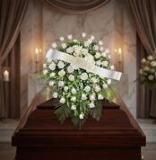 Cubre caja fúnebre Bernardita con rosas blancas y follaje verde sobre un ataúd de madera oscura, en un entorno elegante y sol