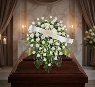 Cubre caja fúnebre Bernardita con rosas blancas y follaje verde sobre un ataúd de madera oscura, en un entorno elegante y sol