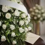 Fotografía macro premium del Cubre Caja Fúnebre Bernardita, con rosas blancas, follaje verde, rocío sutil y cinta satinada. S