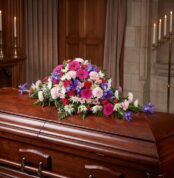 Cubre caja fúnebre "El Legado de Francisco" con flores variadas en tonos rosas, morados y blancos, sobre un ataúd de madera o