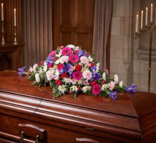 Cubre caja fúnebre "El Legado de Francisco" con flores variadas en tonos rosas, morados y blancos, sobre un ataúd de madera o