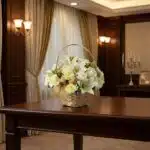 Cubre Caja Fúnebre Elizabeth, un hermoso arreglo floral en tonos blancos con lirios y rosas, presentado en una cesta de mimbr