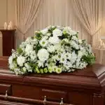 Cubre caja fúnebre Epifania con flores blancas sobre un ataúd de madera oscura, en un entorno elegante y sereno con iluminaci