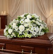 Cubre caja fúnebre Epifania con flores blancas sobre un ataúd de madera oscura, en un entorno elegante y sereno con iluminaci