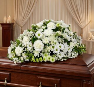 Cubre caja fúnebre Epifania con flores blancas sobre un ataúd de madera oscura, en un entorno elegante y sereno con iluminaci