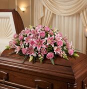 Cubre caja fúnebre Ifigenia con rosas y lirios rosados, eucalipto y follaje verde, elegantemente dispuesto sobre un ataúd de