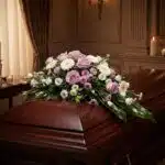 Cubre caja fúnebre "Jardín de Ines" con rosas lilas, margaritas blancas y flores moradas sobre un ataúd de madera oscura en u