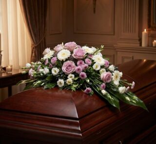 Cubre caja fúnebre "Jardín de Ines" con rosas lilas, margaritas blancas y flores moradas sobre un ataúd de madera oscura en u