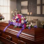 Cubre caja fúnebre 'El Legado de Francisco' con un arreglo floral vibrante de gerberas, claveles e iris, y una cinta morada c