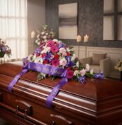 Cubre caja fúnebre 'El Legado de Francisco' con un arreglo floral vibrante de gerberas, claveles e iris, y una cinta morada c