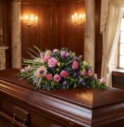 Cubre caja fúnebre 'Legado Sereno de Ivon' con rosas rosadas, claveles y cardos azules sobre un ataúd de madera oscura en un