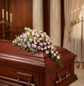 Cubre caja fúnebre elegante con rosas rosadas y follaje verde, delicadamente dispuesto sobre un ataúd de madera oscura en un