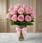 Jarron Allegria con doce rosas rosadas vibrantes y abiertas, adornado con un elegante moño rosa, sobre una superficie de márm
