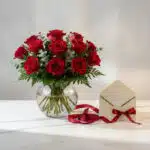 Jarron Floral Graziella con 12 rosas rojas frescas, follaje verde, sobre marmol blanco, con tarjeta de regalo y cinta roja. I