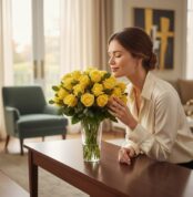 Mujer elegante admirando y oliendo un jarron floral PANDORA con 36 rosas amarillas de lujo en un hogar de alto diseño.