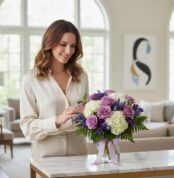 Mujer elegante admirando el Jarron Floral VITTORIA con rosas lilas, hortensias blancas y lavanda, en un interior de lujo.