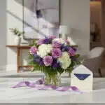 Jarron Floral VITTORIA con rosas lilas, hortensias blancas y flores azules, sobre marmol con tarjeta de regalo y cinta morada