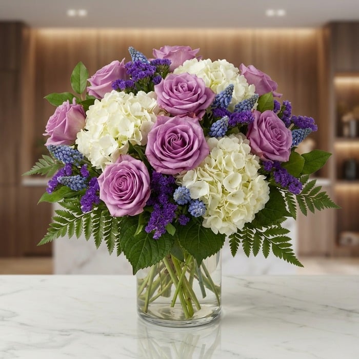 Jarron Floral VITTORIA con rosas lilas, hortensias blancas y muscaris azules, sobre una superficie de mármol en un entorno de