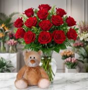 Jarrón Llévame Contigo con un exuberante arreglo de rosas rojas frescas y un adorable oso de peluche sentado al frente, sobre