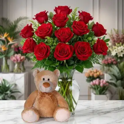 Jarrón Llévame Contigo con un exuberante arreglo de rosas rojas frescas y un adorable oso de peluche sentado al frente, sobre