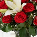 Primer plano extremo de un arreglo floral 'Jarrón Otoño' con rosas rojas vibrantes, lirios blancos y gotas de rocío sutiles,