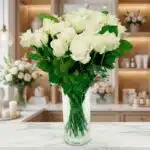 Jarrón de cristal con un gran ramo de rosas blancas frescas y abiertas, sobre una superficie de mármol en un entorno de flori