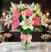 Jarrón Primavera con un exuberante arreglo floral de lirios blancos, gerberas rosas y rosas melocotón, sobre una superficie d