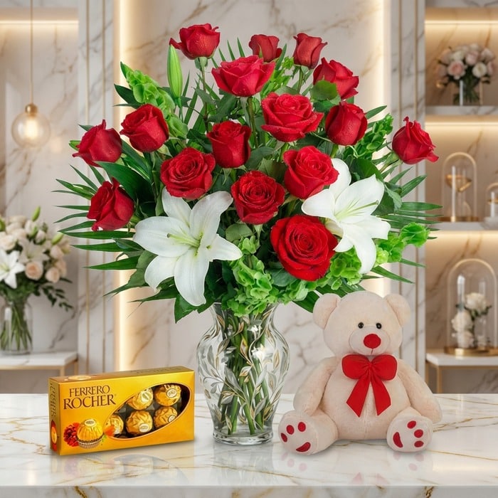 Jarrón Todo Para Ti con un exuberante arreglo floral de rosas rojas y lirios blancos, acompañado de un osito de peluche y cho