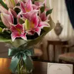 Primer plano de un bouquet fúnebre de lirios Stargazer rosas y blancos con rocío sutil, atado con una cinta verde satinada, s