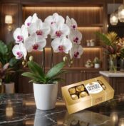 Arreglo floral exótico de orquídea blanca doble vara con centro morado y chocolates Ferrero Rocher en una superficie de mármo